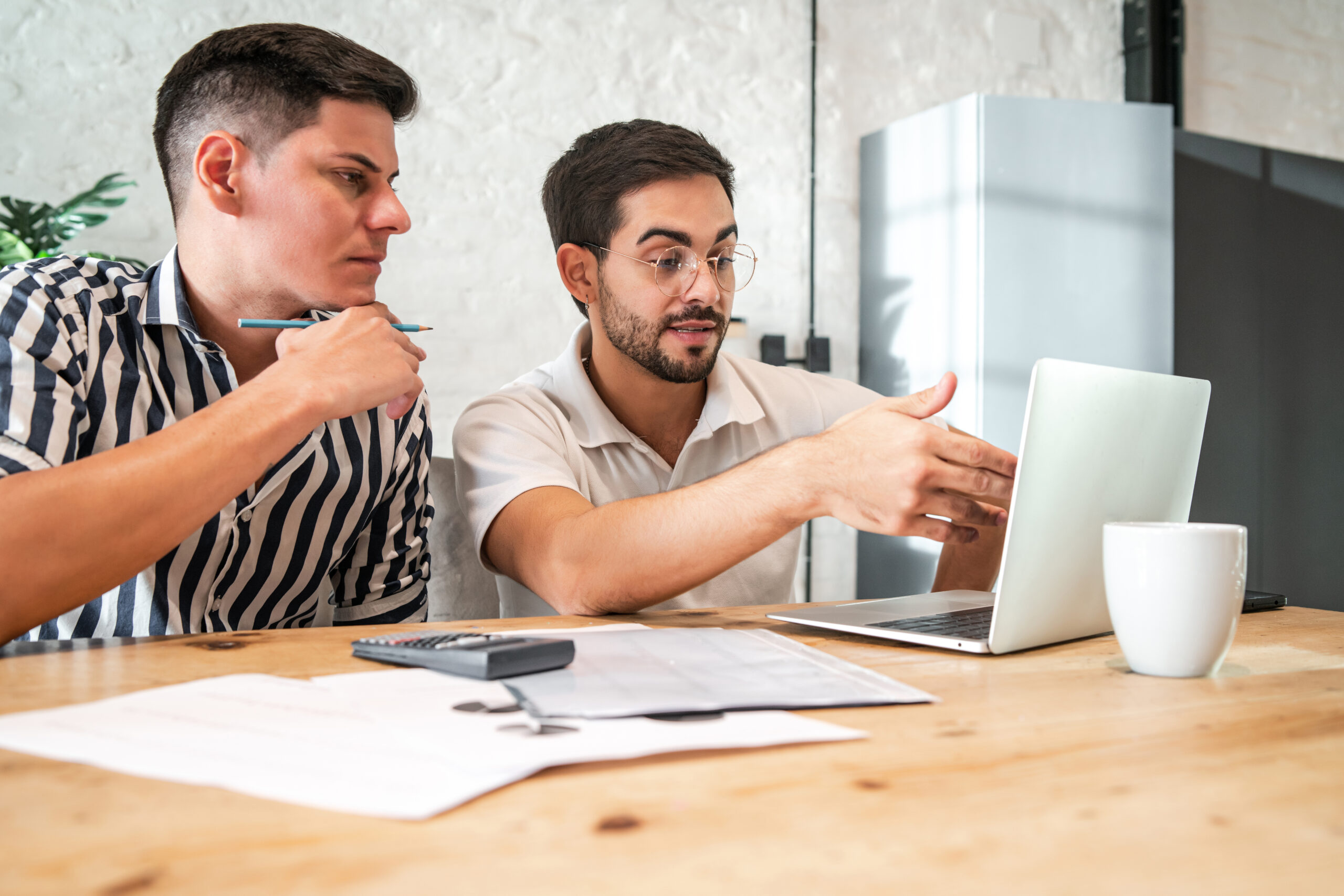 Young gay couple planning their home budget and paying their bills online with a laptop while staying at home. Finance concept.